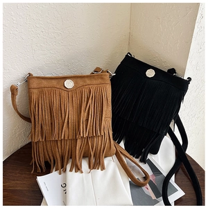 Close-up of bohemian tassel shoulder bags with metallic M logo clasp on wooden table