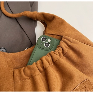 Detail of a brown suede hobo bag with an external pocket holding a green mobile phone