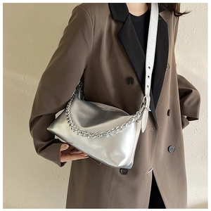 Détail du sac bandoulière argenté métallisé avec chaîne épaisse sur un blazer marron