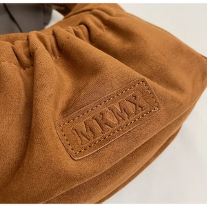 Detail of MKMX embossed logo on a brown suede cloud bag with stylish gathered pleats