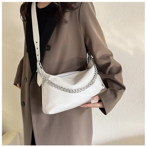 Gros plan d'un sac en cuir verni blanc avec chaîne argentée porté par un mannequin