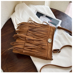 Detail of brown suede crossbody bag with fringe layers and embossed metal logo button