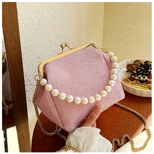 Detail of pink tweed frame bag with pearl handle and gold chain on wooden table