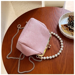 Pink woven handbag with pearl handle and gold chain on a wooden table with dessert