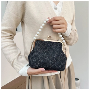 Detail of black glitter clutch with pearl handle and golden chain on beige cardigan