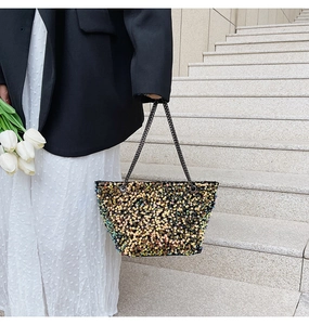 Detail of elegant gold and black sequined tote bag with metal chain straps worn by model