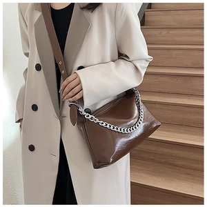 Détail d'un sac bandoulière marron foncé avec chaîne argentée porté par un mannequin