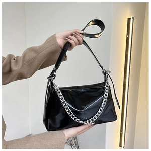 Détail du sac à bandoulière en cuir verni noir avec chaîne argentée tenu par un modèle