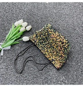 Detail of sequin shoulder bag with colorful gradient and checkered woven strap on pavement