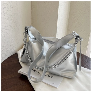 Détail du sac argenté métallisé avec grosse chaîne et texture cuir posé sur une table