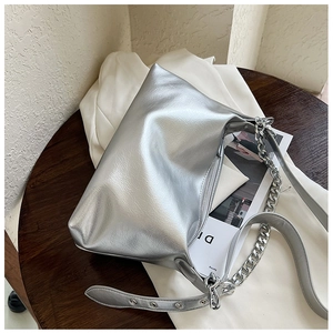 Détail du sac argenté avec une grosse chaîne et une bandoulière en cuir réglable