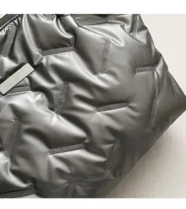 Macro detail of silver quilted metallic tote showing padded texture and silver metal tag