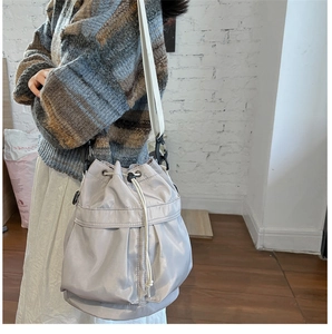 Gray nylon drawstring bucket bag with cream shoulder strap shown in a casual lifestyle setting