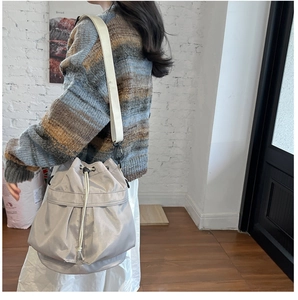 Detailed view of light gray nylon bucket bag with drawstring closure and cream-colored strap