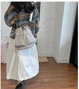 Rear view of a light gray nylon drawstring bucket bag with adjustable white strap