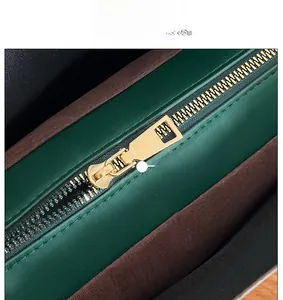 Detailed close-up of premium golden metal zipper closure on a dark green leather tote bag