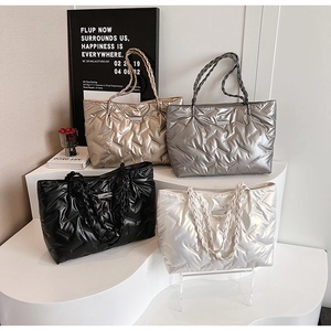 Close-up of metallic quilted tote bags in gold, silver and black on a white display