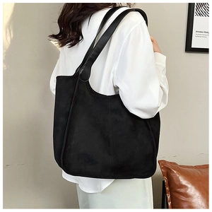 Close-up of a large black suede tote bag shown on a shoulder in a modern room