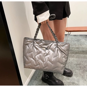 Detail of silver metallic quilted puffer tote bag featuring woven handles and glossy texture