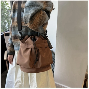 Brown nylon drawstring bucket bag with black strap shown on model in casual style