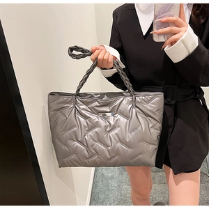 Detail of silver quilted puffer tote bag with thick woven handles held by a model