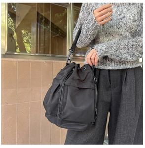 Detail of black nylon bucket bag featuring a drawstring closure and side pockets in outdoor use