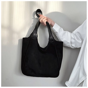 Detail of black suede hobo tote bag featuring a textured finish and smooth leather handle