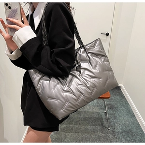 Close-up of a silver quilted tote bag with metallic finish and grey woven handles on a model