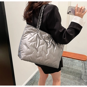 Silver quilted tote bag featuring metallic finish and woven handles shown on a model