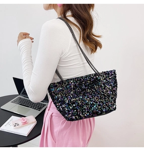 Detail of shimmering black sequin tote bag with metallic chain strap on model shoulder