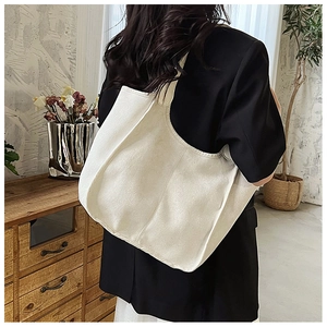 Detailed view of the large off-white canvas tote bag worn over the shoulder by a model