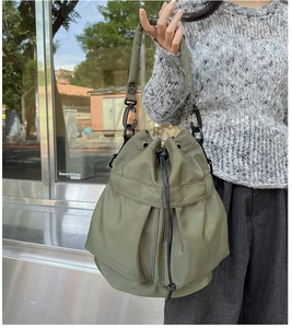 Detail shot of army green nylon bucket bag with drawstring closure on model's shoulder