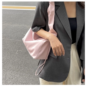 Close-up of a pink satin cloud baguette bag styled on a shoulder with a gray blazer