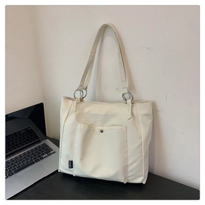 Detail view of large beige canvas tote bag showing outer snap pocket and metal strap rings