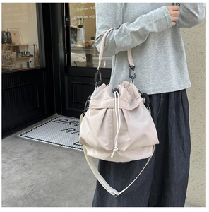 Detail of light pink nylon bucket bag featuring drawstring closure and wide strap