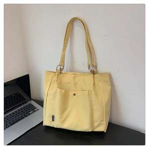 Detail of pale yellow tote bag with silver snap button and brand label on desk