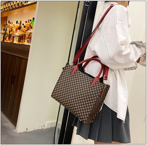 Classic tote bag with vintage monogram pattern and vibrant red handles shown on model