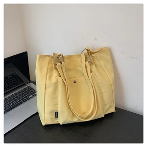 Detailed shot of yellow nylon tote bag featuring a front pocket and silver metal rings