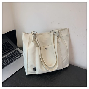 Detail of beige tote bag featuring silver ring handles and external pocket on a desk