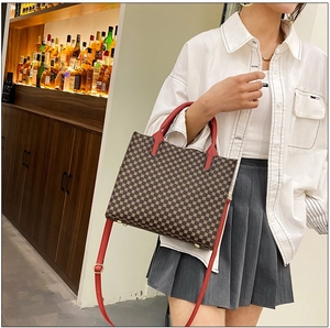 Classic retro monogram tote bag with red handles and gold studs worn by a model