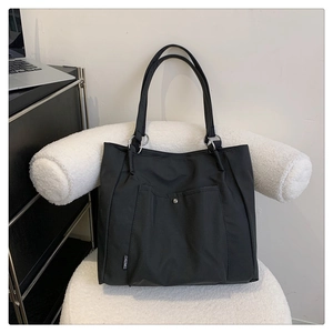 Detail of black nylon tote bag with metal snap pocket and reinforced dual handles