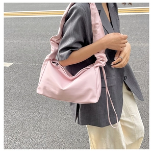 Detailed view of pink pleated shoulder bag with soft twist strap on a model outfit