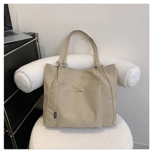 Detail view of beige nylon tote bag featuring front pocket with silver snap and brand label