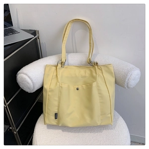Detail of light yellow nylon tote bag featuring a metal button pocket and black brand label