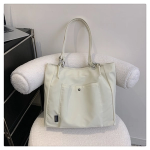 Detail of cream tote bag with buckle pocket and brand tag on a modern white chair