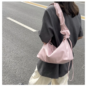 Detailed view of pink pleated dumpling shoulder bag worn by model on an outdoor street