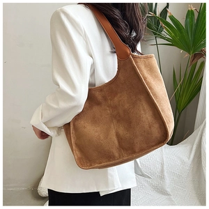 Brown suede tote bag with exposed stitching and leather strap shown on shoulder