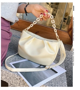 Detail of soft pleated cloud bag with resin and gold metal chain strap on stone surface