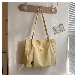 Detail of cream-yellow tote bag with metal snap pocket hanging in natural window light