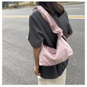Pink pleated dumpling bag with knotted shoulder strap worn over a grey blazer